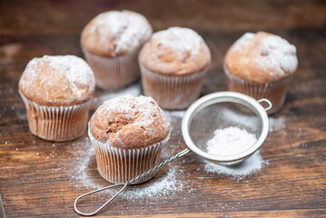 Delicious cupcakes sprinkled with powdered sugar stand on a wooden table