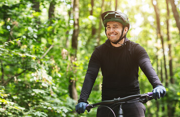 Joyful male bicyclist cycling in mountain forest in sun flares, enjoying the view, copy space