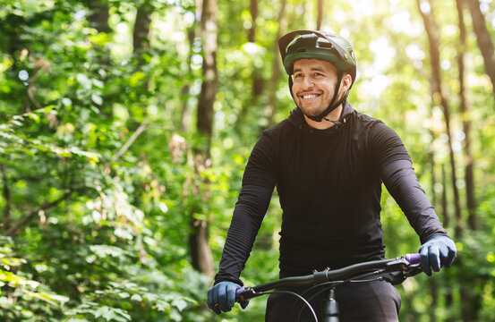 Joyful male bicyclist cycling in mountain forest in sun flares, enjoying the view, copy space