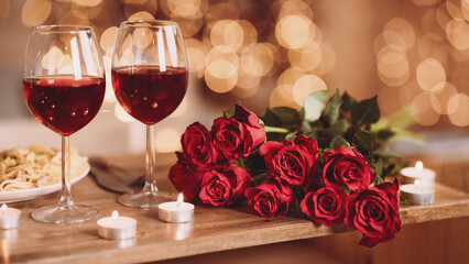 Naklejka na ściany i meble Romantic Dinner. Bouquet of flowers lying on the table, selective focus on bunch of roses, two glasses of red wine and candles on the wooden desk. Date concept, blurred background, banner, copy space