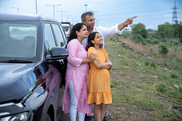 Indian couple showing nature or birds to little girl kid in front of car - concept of family...