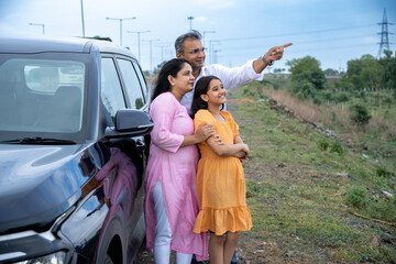 Indian couple showing nature or birds to little girl kid in front of car - concept of family...