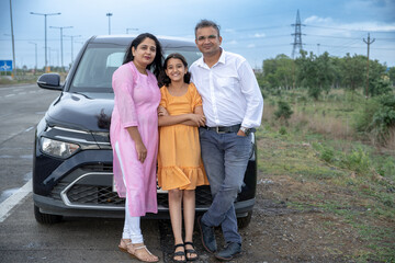 Indian couple showing nature or birds to little girl kid in front of car - concept of family...