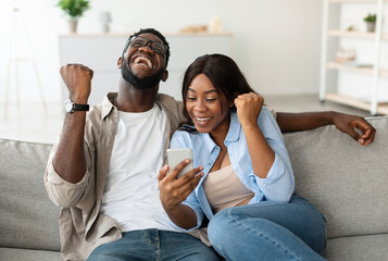 Yeah. Emotional excited black couple celebrating online win, great deal or business success,...