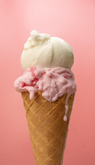 Vertical Front view delicious waffle cone topped with melting scoops of strawberry and vanilla ice cream on pink background. 