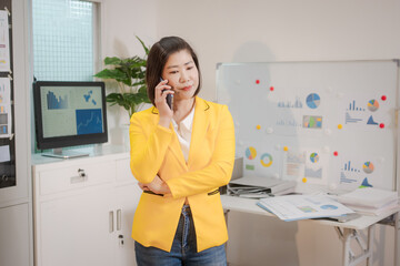 A middle-aged Asian woman sits at a work desk, deeply focused. Surrounded by charts and notes, she...