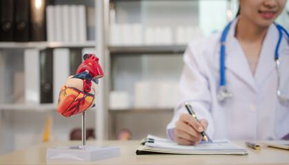 A young Asian female doctor works alone at her desk, reviewing cardiovascular patient records....