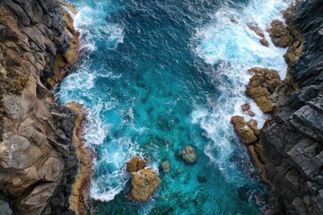 An aerial view showcases a vibrant turquoise ocean inlet nestled between dark, rocky cliffs. White-capped waves crash against the shore, creating a dramatic contrast
