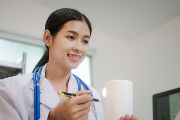 A young Asian female doctor sits alone at her desk, carefully reviewing liver disease.She focuses...