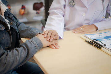 A young Asian female doctor consults with a patient seated across the desk. Using a heart model,...