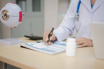 A middle-aged Asian female doctor holds an eye model at her desk, explaining eye anatomy and vision...