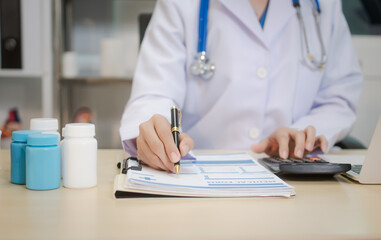 A middle-aged Asian female doctor sits at her desk, pointing to a spinal model with a highlighted...
