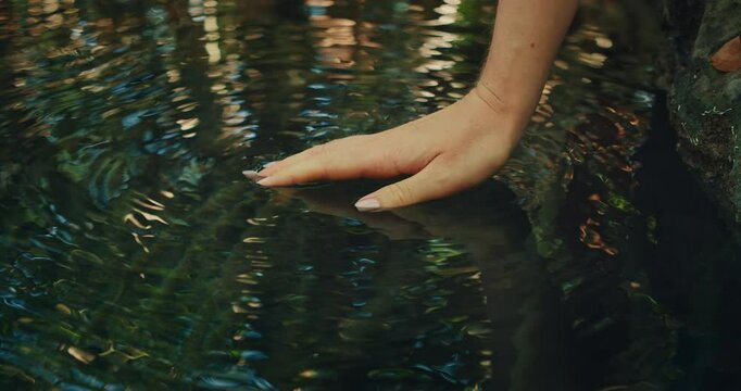 A hand barely touches the surface of a clear rippling pool of cenote in the jungle of Yucatan Mexico