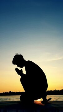 silhouette of a young man praying with his head bowed and