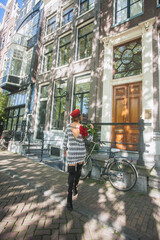 Unrecognisable fashionable woman away from the lance on the streets of Amsterdam. Model is wearing knit dress ,long boots and is holding bouquet of roses in the hand. Fashion travel concept