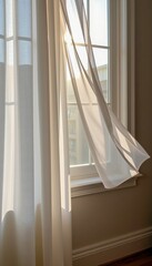 Sheer white curtains gently blowing in the breeze by a sunlit window with a view of an urban building outside.