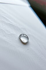 A single clear water droplet rests on a smooth, light-colored wooden surface with soft shadows and reflections.
