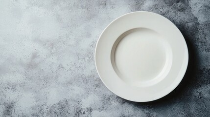 A white plate with a single, empty, round, circular, and smooth surface on a textured, gray, concrete, or stone background.