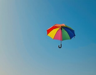 A colorful umbrella with red, yellow, green, and blue panels floats against a clear blue sky.