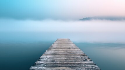 Fototapeta premium A wooden dock extending into a calm, foggy lake with a distant island in the distance.