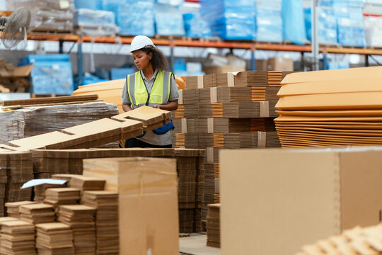 Machine operators work in a large paper factory and check stock of cardboard boxes.