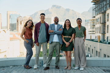 A diverse group of smiling business people standing together on rooftop in city on sunny day