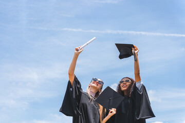 Happy Female Graduates Holding Diplomas and Caps, Joyful Graduates Celebrate Success Under Blue Sky