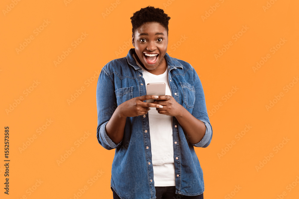 Aufkleber Great Application. Joyful Black Female Using New Smartphone And Mobile App Posing Smiling To Camera Standing Over Yellow Studio Background. Woman Playing Games On Phone Concept