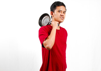Asian man wearing red t-shirt holding frying pan on shoulder with angry 
expression, isolated on...