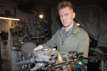 Portrait of young adult Caucasian man assembling and repairing custom motorcycle in workshop,...