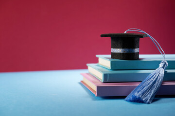 small mortarboard with blue tassel on books against red background