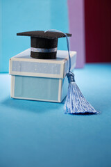 small mortarboard with blue tassel on gift box against blue background