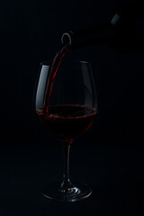 A bottle pouring red wine into a glass at night