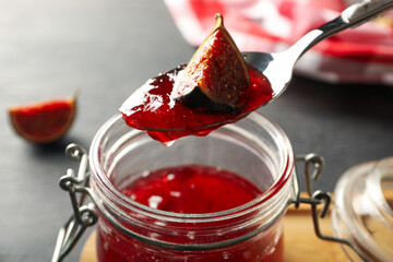 Jar of fig jam and spoon on gray background, close up
