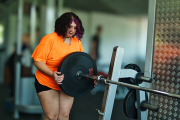 View of an overweight young Latina woman carrying weights and preparing to workout at a gym. Pushing herself. Improvement and well-being.