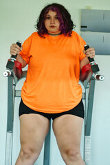 Beautiful overweight Latina woman wearing colorful 80s-style clothing and makeup, exercising with abdominal muscles on a machine in a gym, very positive. Effort, improvement, and overcoming.