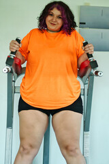 Beautiful overweight Latina woman wearing colorful 80s-style clothing and makeup, exercising with abdominal muscles on a machine in a gym, very positive. Effort, improvement, and overcoming.
