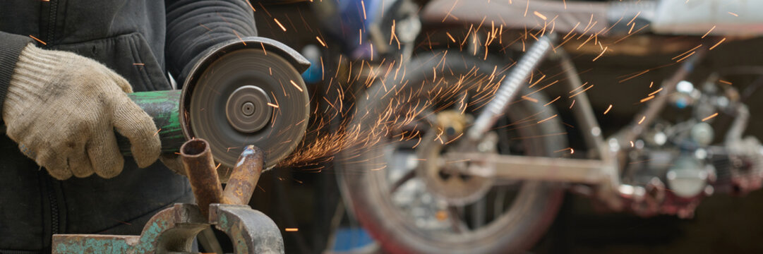 Middle aged Caucasian man using angle grinder while assembling and repairing custom bike in workshop, wearing protective gloves, sparks flying from metal frame, focused on mechanical work - Powered by Adobe