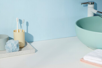 Minimal blue bathroom with green sink, bamboo toothbrushes, and towel stack. Clean surface offers...