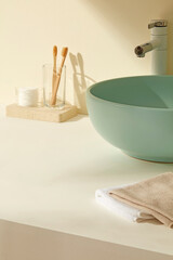 Minimal bathroom surface with bamboo toothbrushes placed in a wooden tray beside a green ceramic...
