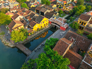 Scenic drone shot of the Japanese Bridge and old town in Hoi An. UNESCO World Heritage Site with historic buildings, rooftop textures, and serene atmosphere. Great for cultural and travel visuals