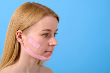 beauty skincare woman uses facial tape for lifting effect against blue background. concept of...