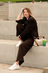 Young woman sitting on stairs holding phone and coffee cup outdoors. Natural feel with soft light....
