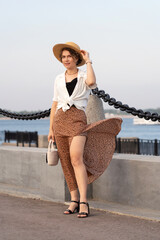 Cheerful woman holding straw hat enjoys breezy waterfront stroll.