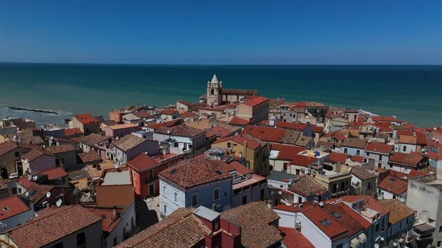 Slow drone descend above Termoli cathedral with vibrant blue seaside and colorful old town rooftops.