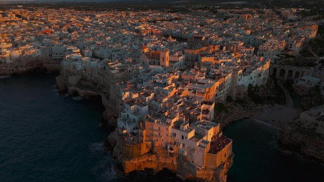 Polignano a Mare by sunset. Famous Lama Monachile beach between high rocky walls and historic old town, Italy.