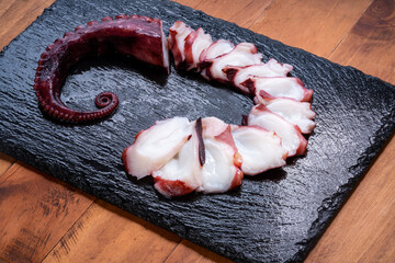 Raw Tentacles of octopus on black plate on white background, kraken tentacles sashimi isolate on white background.