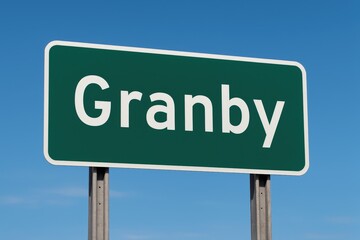 Green road sign with the name Granby, set against a vibrant blue sky, representing city entrance, direction, or travel route.
