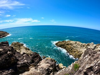 Obraz premium Rocky Coastal Cliffs with Ocean Waves and Blue Sky – Dramatic Seascape with Natural Rock Formations