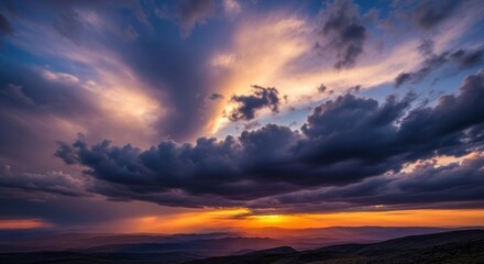 Obraz premium Dramatic Sky Displayed Through Majestic Clouds During Sunset With Golden Rays Peeking Through Over Distant Hills